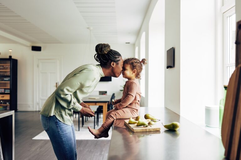 Loving young African mom and her cute little daughter eating a healthy fruit snack together in their kitchen at home